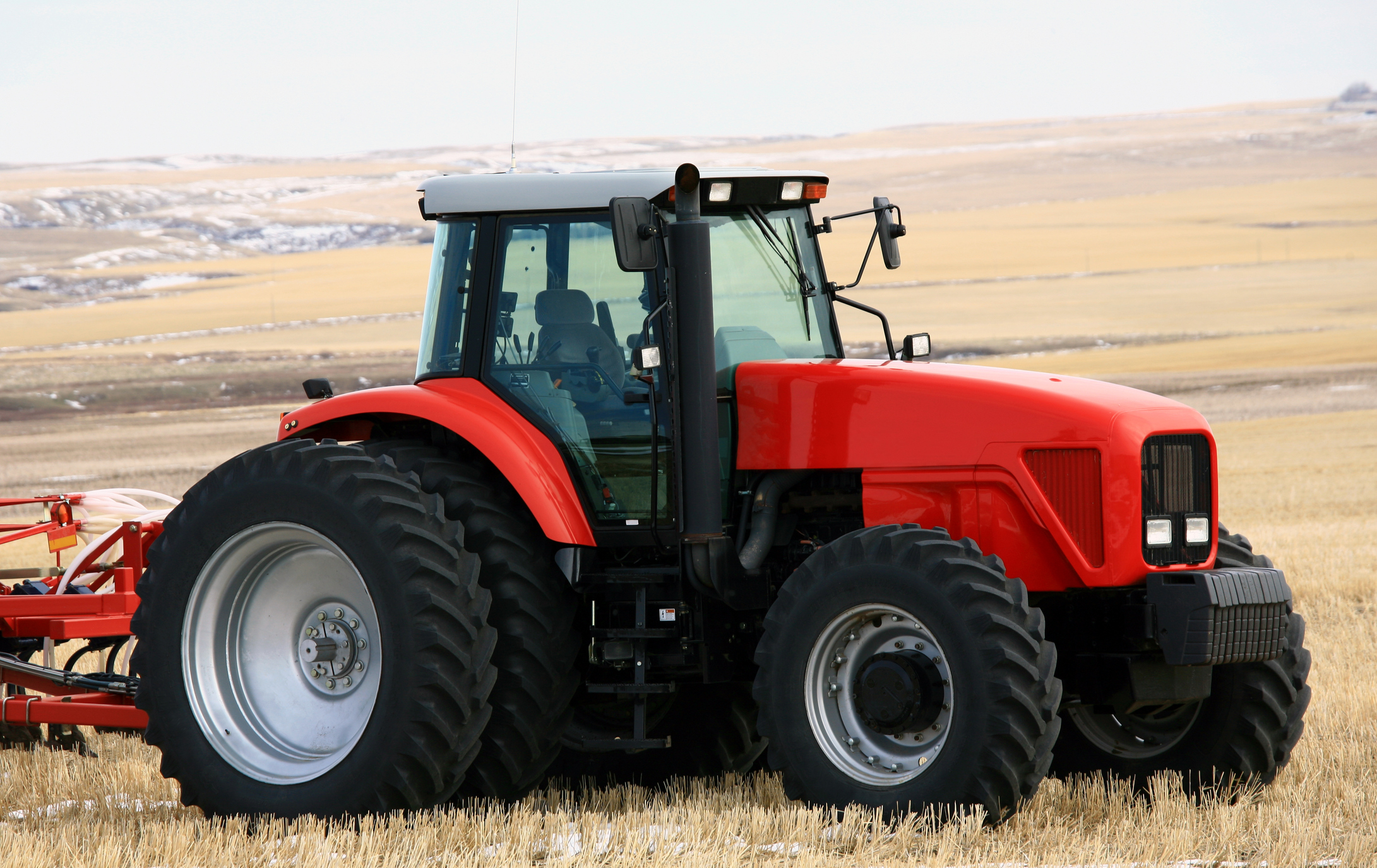 A red tractor with a cultivator is parked in the field.
