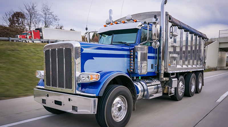 Blue chrome dump truck driving on highway with 18 wheeler in the background