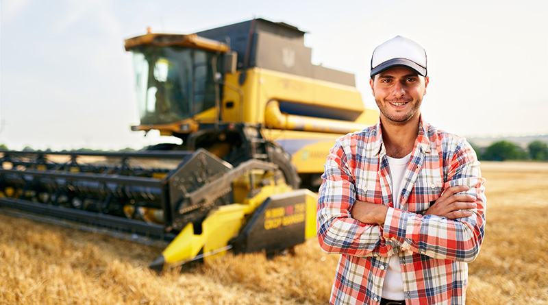 Portrait of proud harvester machine driver with hands crossed on chest. Farmer standing at his combine. Agronomist looking at a camera. Rancher at harvesting work on stubble of harvested wheat field.