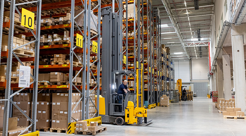 Big warehouse area with forklift loader moving boxes. Industrial warehouse with boxes stored on large racks and forklift working