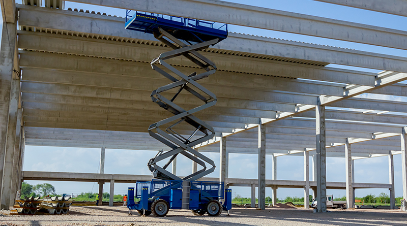 Scissor lift platform with stretched hydraulic system at maximum height range under building skeleton.